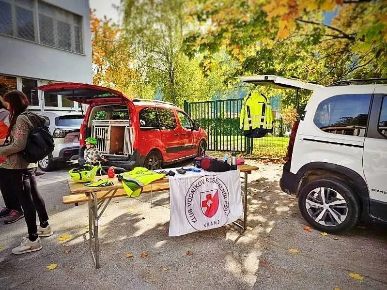 Predstavitveni prostor kluba: miza z opremo in klubsko zastavo, ob njej avtomobil s pasjimi boksi.