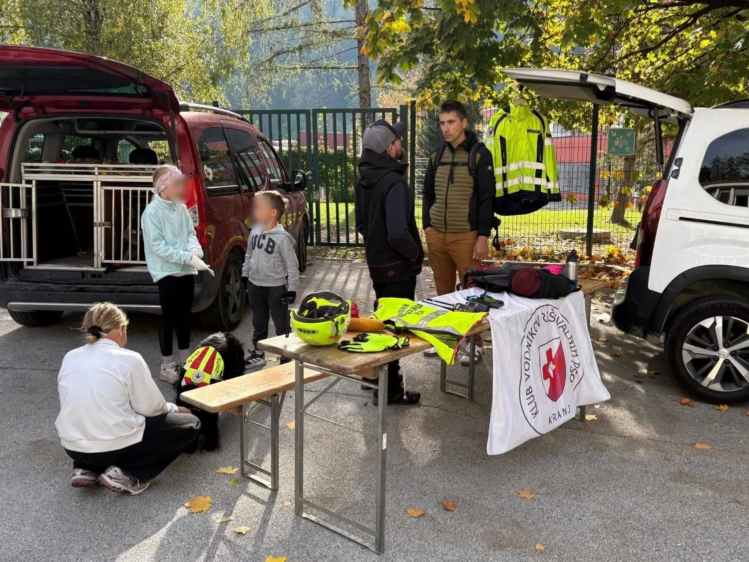 Otroci in obiskovalci ob reševalnem psu in mizi z opremo.
